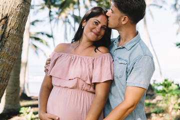 Happy pregnant couple hugging in tropical park