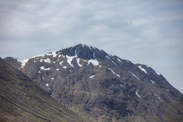 Snow-capped mountain peak in the Scottish Highlands surrounded by dramatic landscapes beneath a cloudy sky