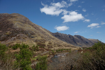 Scenic view of the rugged Scottish Highlands with rolling hills and a winding river under a clear blue sky