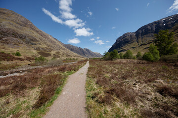 Stunning view of a trail winding through the scenic valleys of Scotland under a clear blue sky during daylight hours