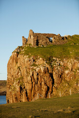 Ruins of an ancient castle perched atop rugged cliffs along the coastline of Isle of Skye in...