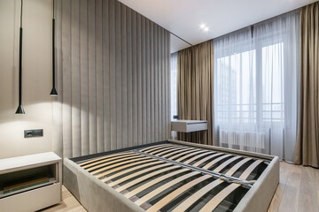 A bedroom in an apartment with an elegant interior design. A window with beautiful curtains. Soft covering of the wall at the head of the bed with a lifting mechanism.