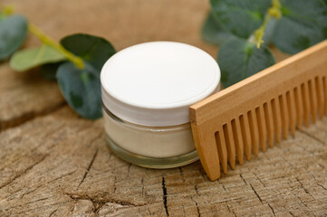 Cosmetic cream in a glass container. On a wooden background. Wooden comb.