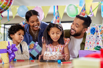 Little girl celebrating birthday with family while blowing out candles