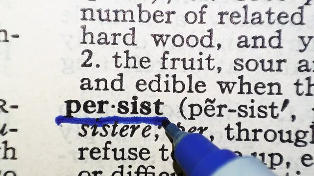 A man marks the definition from the word persist on a printed page with a pen