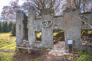 The remnants of the historic Konigsmuhle settlement showcase crumbling walls and a heart decoration. Nestled in the Ore Mountains of Czechia, nature slowly reclaims this once vibrant area.