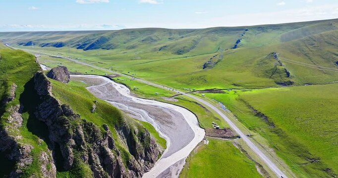 Aerial view of curving river and highway road with green grassland on a sunny day. Beautiful scenery along the Duku Highway in Xinjiang, China.