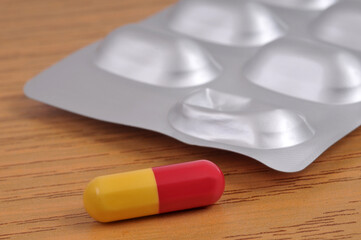 Gélule rouge et jaune à côté d'un blister de médicaments sur un fond en bois