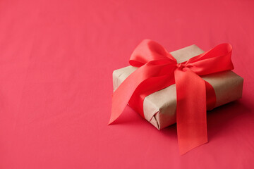 gift box wrapped in craft paper and red bow on red background