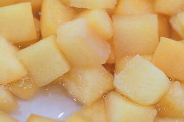A close up of a pile of yellow pineapple fruit cubes. The fruit cubes are frozen and appear to be cut into small pieces. Concept of abundance and freshness