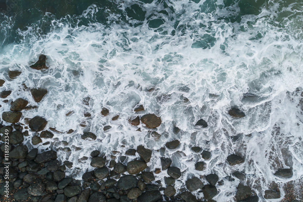 Poster a rocky shoreline with a large wave crashing against the rocks. the water is white and frothy, and t