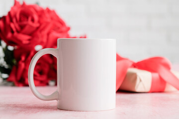 White mug mockup with roses and gift boxes in the background