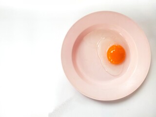 Duck egg yolk on a pink plate on a white background.