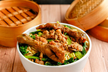 Chicken noodle with chicken foot or usually it's called mie ayam in Indonesia on a wooden table in white bowl with dimsum klakat or mushiki. It's has chili sauce on a mini bowl