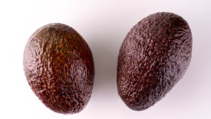 Two avocados are sitting on a white surface. They are both brown and have a rough texture