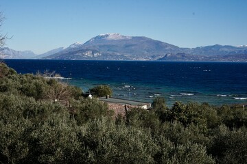 Beautiful view of Lake Garda with waves, lush greenery in the foreground, a small pier, and mountains near Verona.