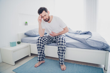 Photo of depressed sad mature guy dressed sleepwear feeling head pain sitting bed indoors room home...