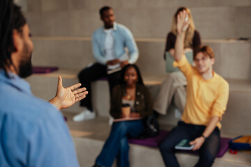 Professor gesturing while explaining to students raising hands in classroom