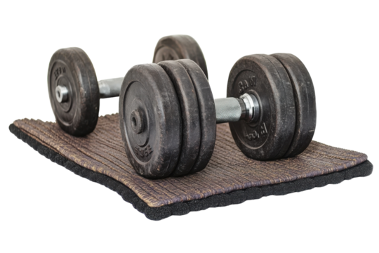 A pair of heavy dumbbells resting on a textured mat in a home gym setting during early morning
