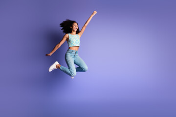 Joyful young woman in stylish summer outfit with afro hair jumps happily against purple background