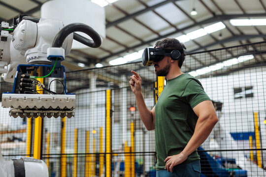 Industrial engineer wearing virtual reality headset controlling robotic arm in factory