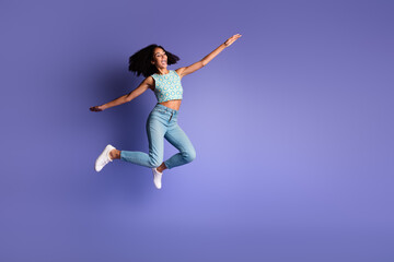 Energetic young woman leaping against vibrant violet background, expressing joy and freedom in stylish summer attire.