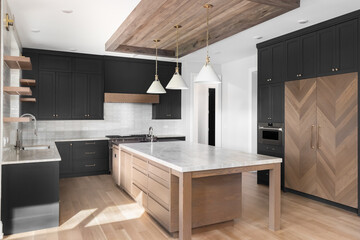 A luxury black detail kitchen with pendant lights and wood frame over a large island, stainless steel appliances, white tiled backsplash, and a white oak wood panel refrigerator. No brands or labels.
