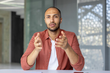 Webcam view, serious and concentrated man looking into the camera talking with colleagues at an...