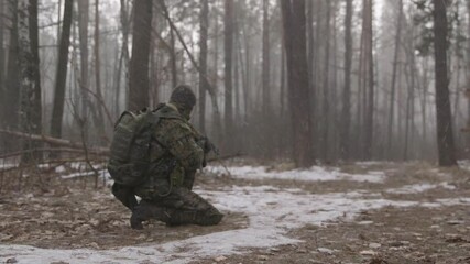Special forces in forest. Armed reconnaissance soldier in winter forest. Infantryman makes his way through a snowy forest. Soldier in Snow Covered Terrain Training for Cold Weather Military Maneuvers.