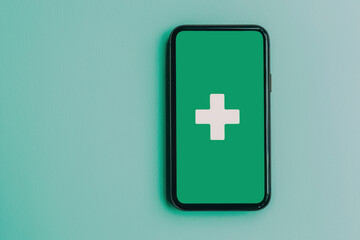 Obraz premium A smartphone with a green screen featuring a white medical cross symbol, set against a minimalist background.