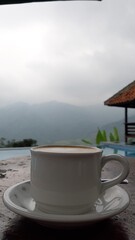 A cup of coffe ona table with a view of pool and mountain