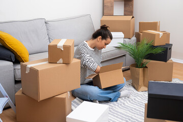 Fresh Start: A woman, new homeowner or renter, sits among boxes, opening packages in her brand-new space, symbolizing new beginnings