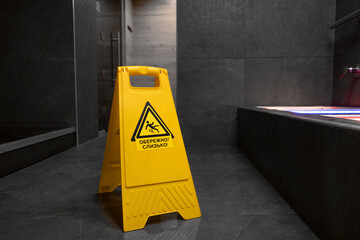 Warning sign Wet floor. Wet floor in the pool. Sauna. Bath. Moisture. Yellow color. Plastic sign. Gray floor. Tile. Yellow warning triangle on the floor with a black warning sign