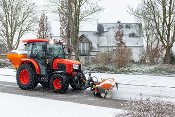 a tractor with a nozzle for snow removal working on a city street against the background of a modern building. The concept illustrates winter road maintenance in urban infrastructure.