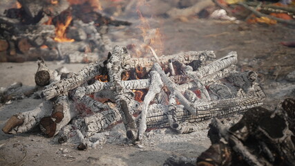 Cremation site with burning wooden pyres and ashes, symbolizing the cycle of life and death