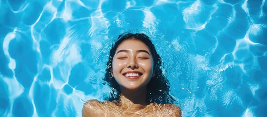 Happy Asian woman relaxing and smiling in an outdoor swimming pool, water glistening under sunlight, enjoying a vacation, summer, leisure, lifestyle, joy, tranquility.