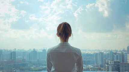 Thoughtful young businesswoman in white shirt, back view, gazing at panoramic cityscape from modern office, bright blue sky with clouds, inspiration and success concept.