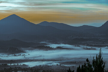 morning on a foggy mountain, city foggy view in mountain,  Landscape photography of view in mountain, A scenic view capturing the early morning fog enveloping a peaceful rural village and surrounding 