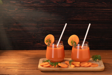 On the cutting board are two glasses with freshly squeezed juice and straws. Carrots and leaves that have been sliced. The sun's rays illuminate the wooden background.