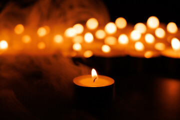 Bright single candle with glowing bokeh candlelights in dark