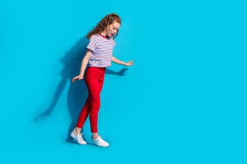 Joyful child in red pants and striped shirt dances against vibrant blue background