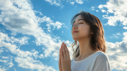 Young asian woman praying to god, thankful and grateful spiritual lady, christian religion or faith. blessed and hopeful in her belief,standing outdoors on a sunny day,blue sky,mental health, positive