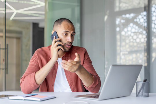 Serious focused man talking on the phone while sitting at a desk inside an office with a notebook, office worker businessman in a casual shirt.