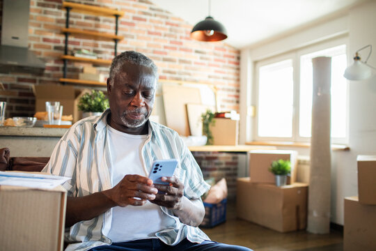 Senior man on phone reviewing paperwork at home with moving boxes