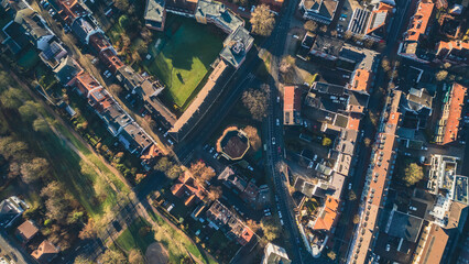 Obraz premium Aerial view of city blocks with red roofs and green areas. The image shows a sunny day, narrow streets and neat houses surrounded by trees. Ideal for illustrating urbanism or architecture.