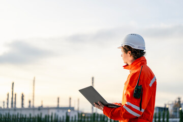 Industrial professional in safety attire analyzing refinery operations using modern technology, showcasing leadership and expertise in industrial safety and infrastructure projects.