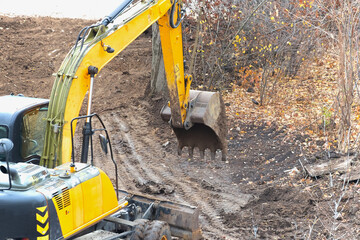 Fototapeta premium Excavator with raised boom at a construction site on an autumn day, excavator work at the very beginning of construction.