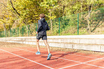 Obraz premium Male athlete in sportswear jogging at outdoor stadium on a sunny autumn day. Healthy and active lifestyle concept.