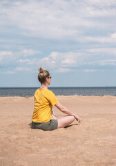 Beautiful woman sits alone on a sandy beach under a serene sky