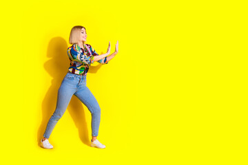 Full length photo of lovely young lady push wall empty space dressed stylish colorful garment isolated on yellow color background